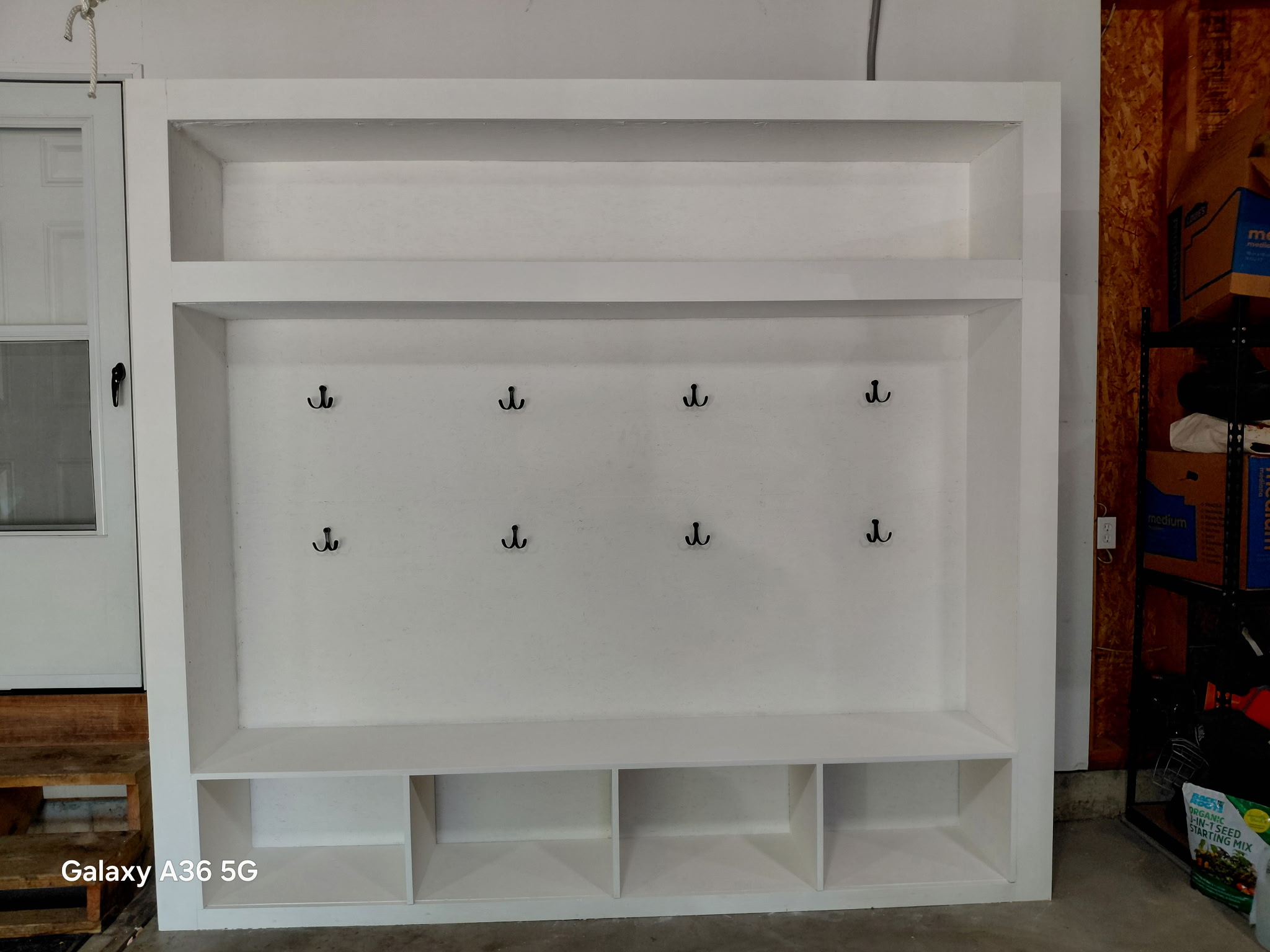 Custom-built white mudroom locker system with coat hooks, bench, shoe cubbies, and upper storage shelf